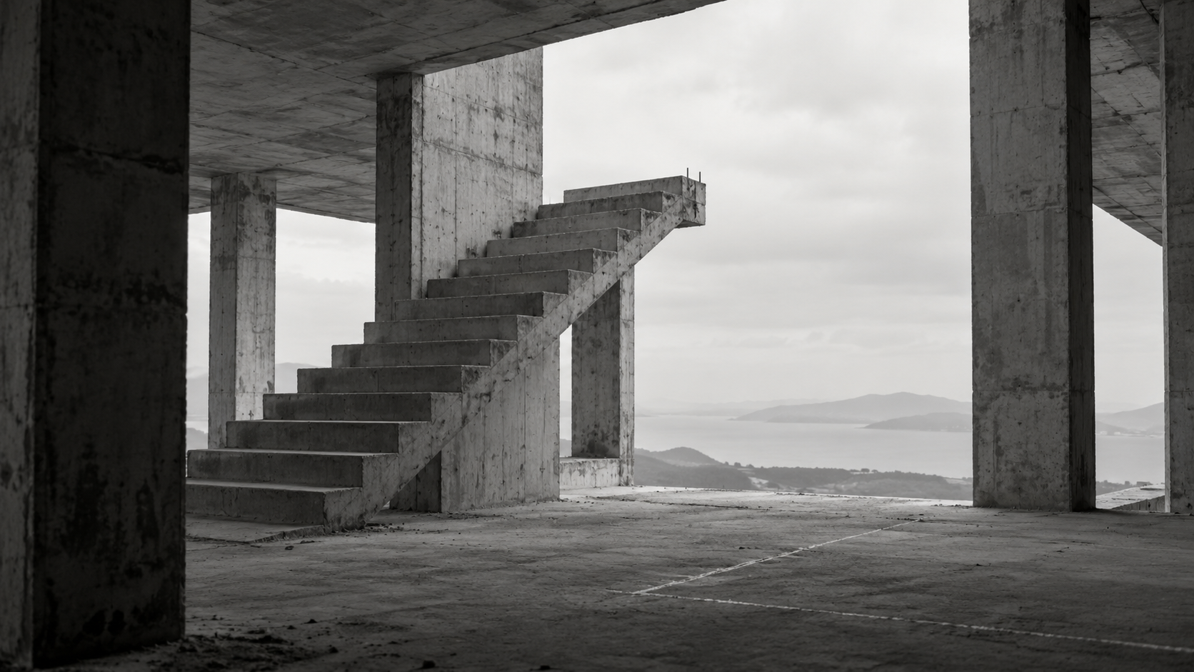 An unfinished concrete staircase ends in open air inside a building overlooking the sea.